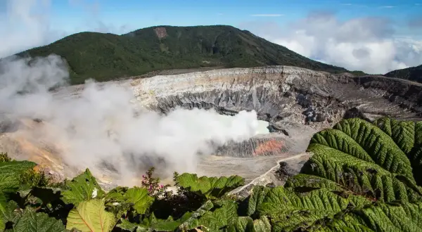Vulkanen Poás i Costa Rica med sin turkosa sjö och ångande krater, omgiven av frodig grönska.