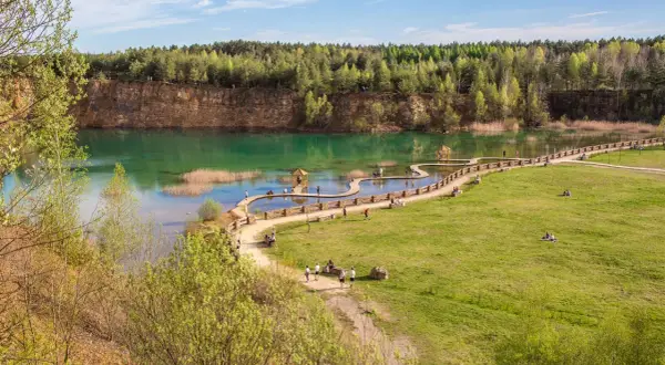 Malowniczy park Gródek Jaworzno z turkusową wodą, drewnianymi kładkami i zielonymi terenami rekreacyjnymi.