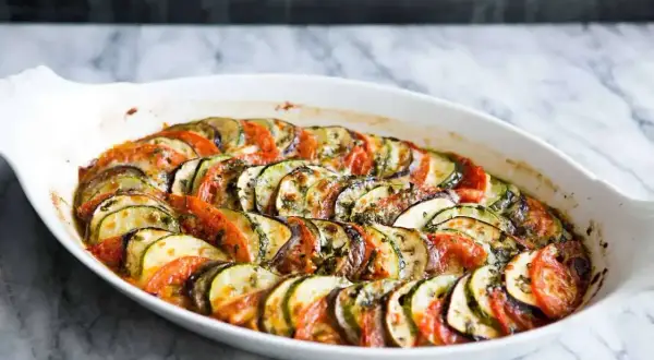 En ugnsbakad ratatouille med skivade tomater, zucchini och aubergine, ett perfekt exempel på enkla vegetariska recept.