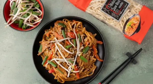 Gotowy do przygotowania dania z makaronem chow mein, który jest idealny do ramen. Na talerzu danie z warzywami i mięsem, obok miseczka kiełków i opakowanie makaronu.