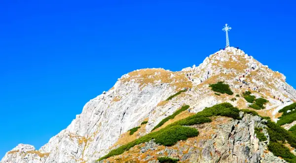 Giewont z Zakopanego, majestatyczny szczyt z krzyżem, na który wspina się grupa turystów.