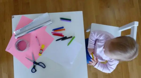 Dziecko przygotowuje materiały do zrobienia lustra z folii aluminiowej: kredki, nożyczki, taśmę, papier i folię.