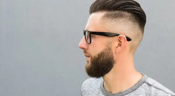 Mężczyzna z zarostem i modnym buzz cut, który sprytnie maskuje zakola.