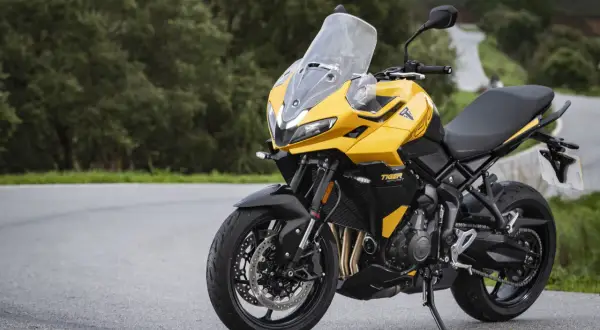 Żółty motocykl uniwersalny Triumph Tiger Sport 660 na krętej drodze wśród zieleni.