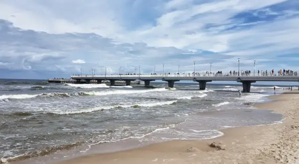 Kołobrzeg wczasy z wyżywieniem: spacer po molo, fale na plaży i tłumy turystów. Idealne miejsce na relaks nad Bałtykiem.