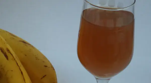 Dwa dojrzałe banany obok kieliszka z bursztynowym płynem, być może domowym winem bananowym.