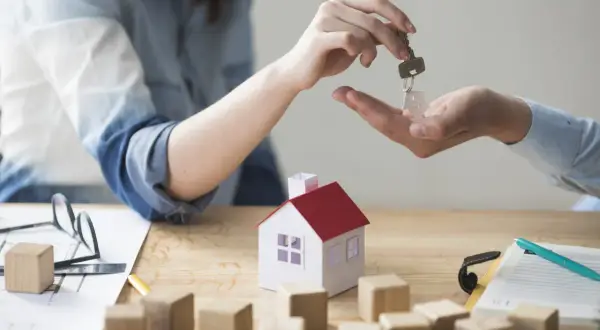 Mani che si scambiano una chiave con un ciondolo a forma di casa. Dopo lo sfratto devo pagare per questo nuovo inizio.