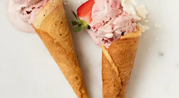 Zwei Waffelhörnchen mit cremigem Erdbeereis und zerbrochenem Baiser.
