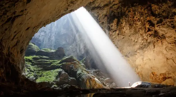 Promień słońca wpada do jaskini Son Doong, oświetlając zielone mchy i skalne tarasy.