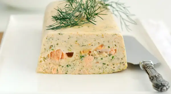 Elegancka terrina z łososia, ozdobiona gałązką koperku, prezentuje się apetycznie na białym talerzu.