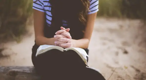 Kobieta z dłońmi złożonymi nad otwartą Biblią, w ciszy szuka siły i spokoju. To jej modlitwa o dobry dzień w pracy.