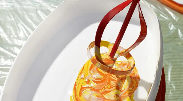 Ein roter Rührer mischt leuchtend gelbe und orangefarbene Wandfarbe in einem weißen Eimer.