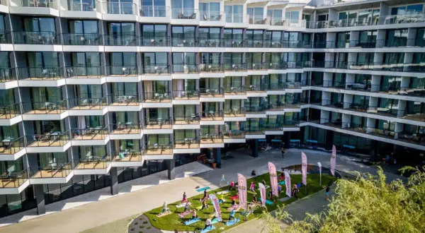 Grupa osób ćwiczy jogę na trawniku przed nowoczesnym seaside park hotel.