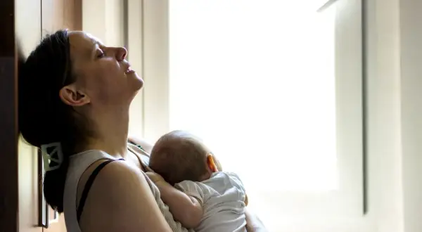 Zmęczona mama tuli śpiące dziecko. Czas po porodzie bywa trudny, ale miłość do malucha daje siłę.