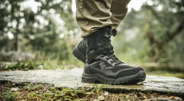 Czarne buty trekkingowe na mokrej kamiennej ścieżce w lesie.