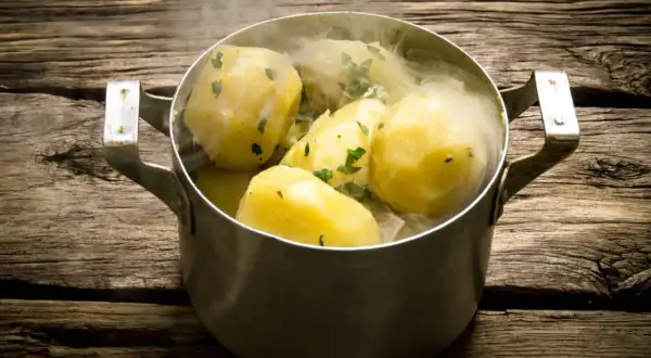Gorące, gotowane ziemniaki w garnku, posypane natką pietruszki. Idealne, gdy zastanawiasz się, ile gotować ziemniaki, by były miękkie.