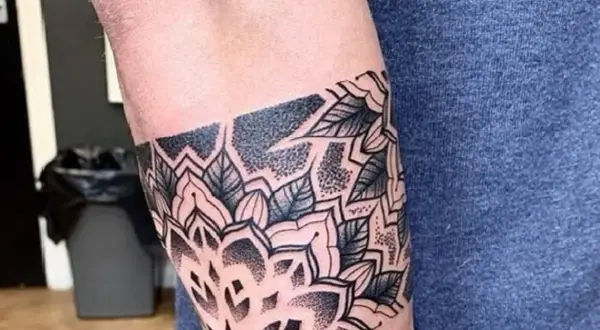 Eleganckie tatuaże męskie na ramieniu w stylu mandali, z motywami liści i geometrycznymi wzorami, wykonane techniką dotwork.