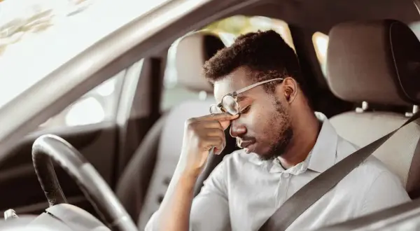 Erschöpfter Mann mit Brille reibt sich die Augen, während er im Auto sitzt. Die lange Fahrt ermüdet ihn.