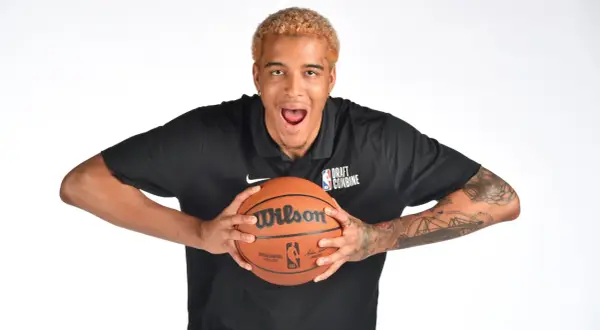 Młody polak w NBA, z blond włosami i tatuażami na ramionach, trzyma piłkę do koszykówki.