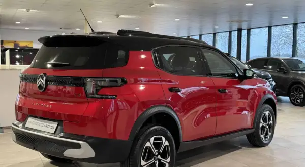 Błyszczący czerwony Citroën C3 Aircross z czarnym dachem stoi w salonie.