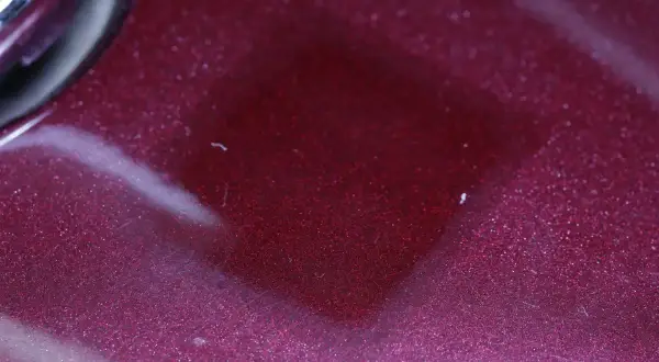 Superficie metallizzata color bordeaux con riflessi scintillanti. Il trasparente è un colore che cattura la luce, creando un effetto quasi liquido.
