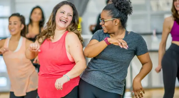 Zwei Frauen lachen und tanzen ausgelassen bei einem Zumba-Kurs. Ein toller Weg, um den **Zumba Kalorienverbrauch** zu steigern und Spaß zu haben!