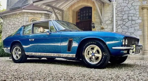 Blå Jensen Interceptor parkerad framför ett stenhus.