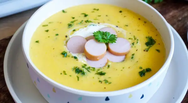 Cremige Kartoffelsuppe, zubereitet im Thermomix, garniert mit Würstchenscheiben, einem Klecks Sahne und Petersilie.