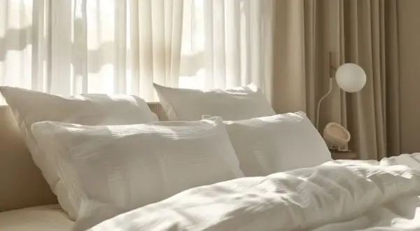 Gemütliches Bett mit weißen Kissen und Decken. Die sanften Falten der Bettwäsche lassen vermuten, dass sie aus einem Material wie Polyester ist, das überraschend warm halten kann.
