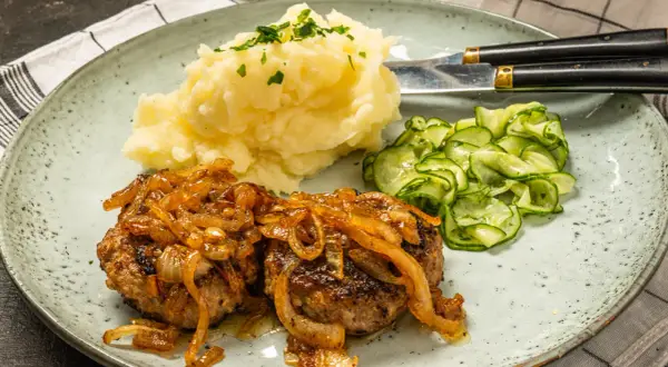 Två saftiga pannbiffar i ugn med karamelliserad lök, serverade med krämigt potatismos och gurksallad. En klassisk svensk rätt.