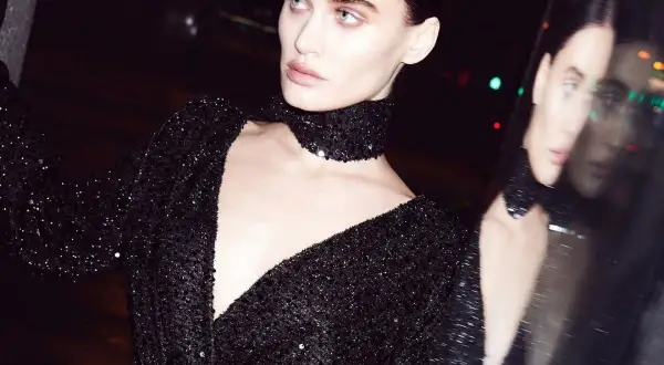 Modelka w czarnej sukience z cekinami i chokerem, odbijająca się w lustrze.