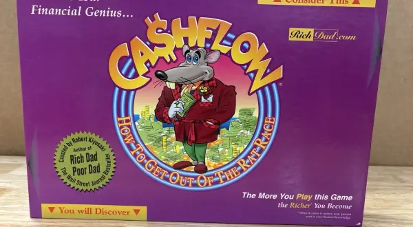 Das Cover des **Cashflow Spiels** zeigt eine Maus in einem Anzug, die Geld hält. Es ist ein Brettspiel, das finanzielle Bildung vermittelt.