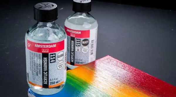 Due flaconi di vernice acrilica Amsterdam, uno lucido e uno opaco, accanto a una tavolozza arcobaleno. Ricorda che la vernice acrilica è tossica.