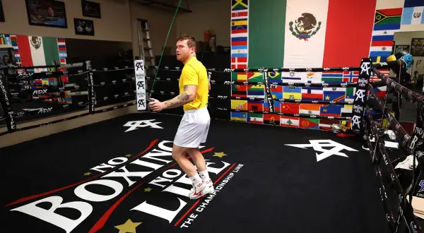 Boxer in yellow shirt doing a boxing jump rope workout in a ring decorated with flags.