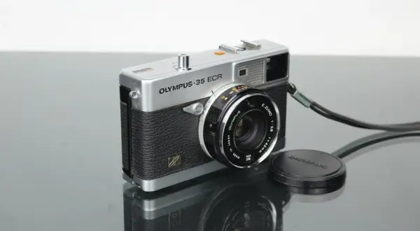 A vintage silver Olympus 35 ECR rangefinder camera with a black textured grip sits on a reflective surface.