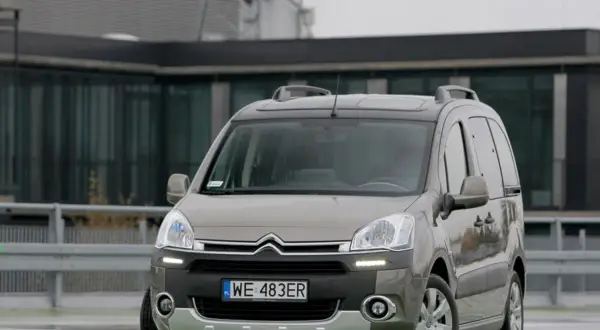 Szary Citroen Berlingo 1.6 HDI z relingami dachowymi zaparkowany przed nowoczesnym budynkiem.