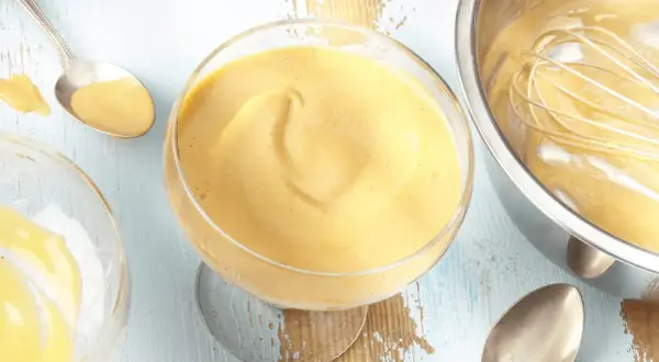 Cremiges Zabaione-Rezept in einem Glas, Löffel daneben. Ein Schneebesen ruht in einer Schüssel mit der köstlichen Masse.