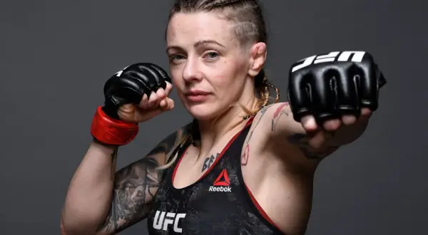 Joanne Calderwood, en MMA-fighter med flätor och tatueringar, visar upp sina boxningshandskar redo för strid.