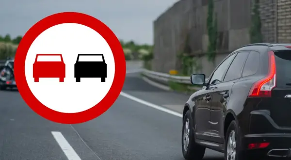 Znak zakazu wyprzedzania na drodze jednokierunkowej. Czarny SUV jedzie po drodze, gdzie wyprzedzanie jest zabronione.