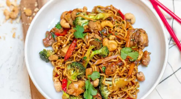 Enkel mat: en skål med nudlar med kyckling, broccoli, paprika och cashewnötter. Röd pinnmat ligger bredvid.