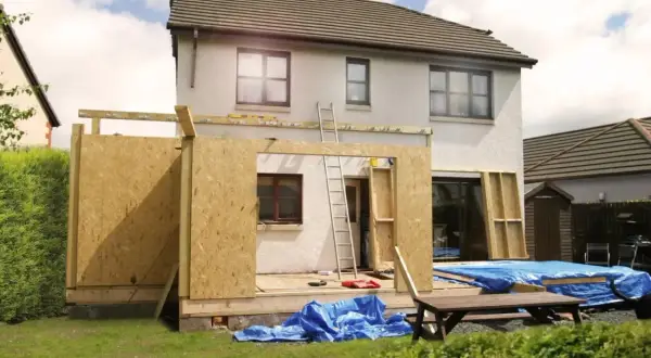 Ein **Anbau Haus** im Bau. Holzkonstruktion und OSB-Platten bilden die Wände des neuen Gebäudeteils. Blaue Planen schützen Baumaterialien.