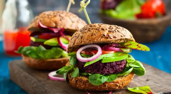 Zwei saftige vegane Burger mit Rote-Bete-Patty, Avocado, Tomate und Zwiebeln auf Vollkornbrötchen – perfekt für vegan zunehmen!