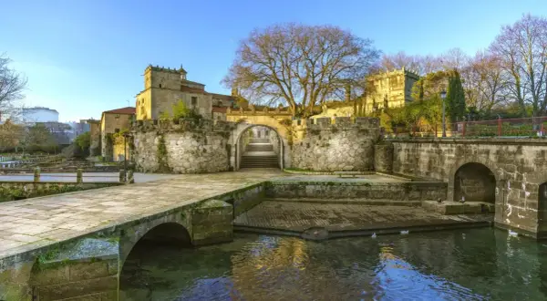 El pazo Vista Alegre, con su puente de piedra y río, se alza majestuoso bajo un cielo azul.