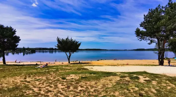 Słoneczny dzień nad jeziorem Pławniowice. Ludzie odpoczywają na piaszczystej plaży, ciesząc się błękitem nieba i spokojną wodą.