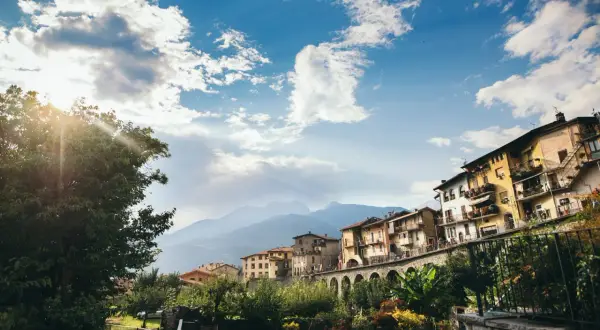 Case colorate si affacciano su un fiume, incorniciate da montagne e cielo azzurro. Un incantevole scorcio dei borghi di Brescia.