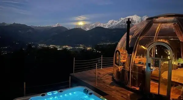 Un jacuzzi illuminé et une bulle transparente, un logement insolite montagne offrant une vue spectaculaire sur les sommets enneigés et la vallée scintillante.