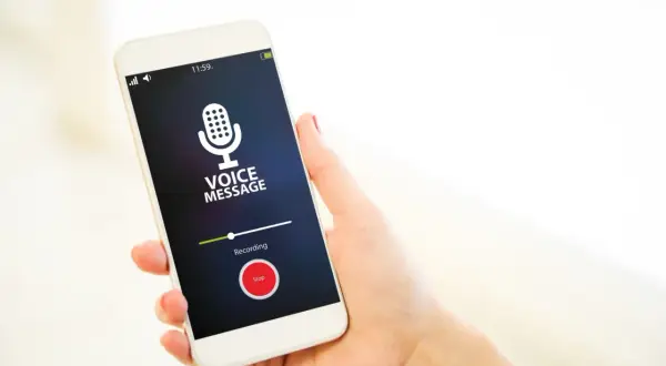 Dłoń trzyma smartfon z włączonym dyktafonem w telefonie. Na ekranie widnieje ikona mikrofonu i napis "Voice Message".