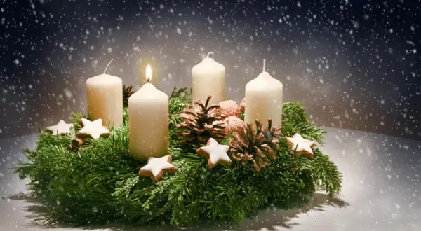 Ein Adventskranz mit vier Kerzen, Tannenzweigen, Zapfen und Sternen. Die erste Kerze brennt. Der Ursprung des Adventskranzes liegt im 19. Jahrhundert.