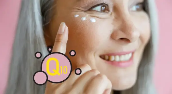 Mujer sonríe mientras se aplica crema en el contorno de ojos. El Q10 es un ingrediente clave para el cuidado de la piel.
