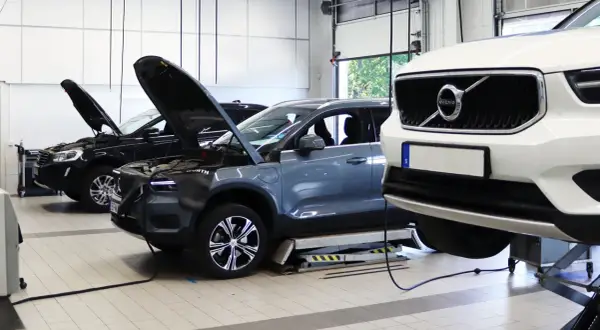 Flera Volvo-bilar, inklusive en vit XC40 och en grå elbil, på verkstad för volvo classic service. Motorhuvar öppna för inspektion.